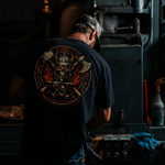 Person wearing a black t-shirt with a graphic design, working on machinery in a workshop.