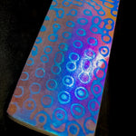 Close-up of Nebula damtanium billet with ringed nebula-style pattern and iridescent anodized finish, 20 layers Grade 2 + 20 layers Grade 5 titanium.