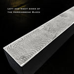 A rectangular block of stainless herringbone pattern damascus showing its top surface, shown at an angle against a dark, textured background.