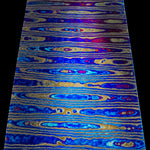 a billet of Ladder pattern zirmascus also known as black timascus or zircuti featuring bright blue, grey and yellow colors on a black background