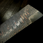 a flat bar of san mai made with layers of copper, carbon steel and nickel laying on a dark wood floor