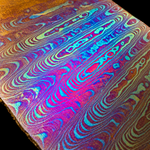 close up image of titanium damscus pattern with bright red and blue and orange colors on black background