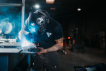 man welding damascus steel while wearing a black t shirt with a white vegas forge logo on the front and white American flag on the right sleeve