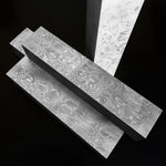 Three rectangular blocks of gray patterned damascus steel material with a wavy, woodgrain-like surface, arranged on a black background.