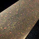 a mokume gane billet with flowing layered patterns of copper, brass and nickel-silver on a black wood background