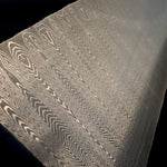 Close-up of a damascus steel billet with intricate sharktooth pattern on a black background