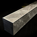 A rectangular block of stainless damascus twist pattern, showing dramatic black and white grain transitions, photographed on a dark background.