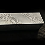 A rectangular damascus steel block with a textured damascus pattern, shown on a dark background.