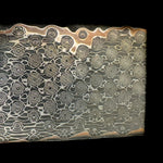 A close-up image of a copper infused San Mai billet with a patterned texture.