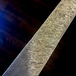 Angled view of a Vortex Damascus steel billet with fine layered lines and repeating swirls against a dark background.