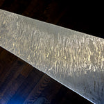 Vortex Damascus flat bar by Vegas Forge, showing bright flowing layers and oval swirls across the gray steel surface.